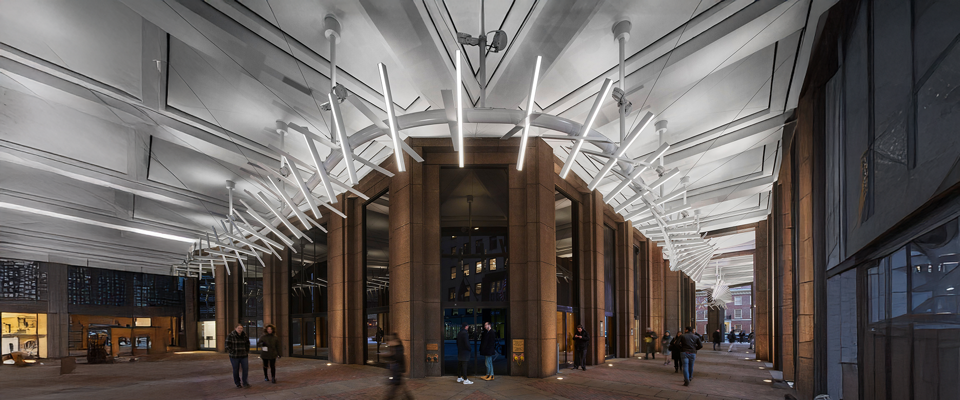Wide-angle view of a modern building entrance at night, featuring angular architecture and bright, linear ceiling lights. People walk past in motion blur, creating an urban, dynamic atmosphere.